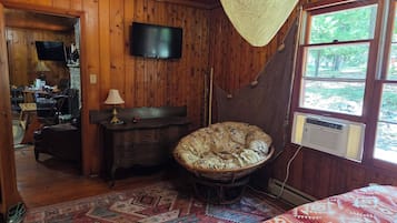 L’intérieur d’un chalet en bois comprend un lit, un téléviseur, un hamac et une grande fenêtre.