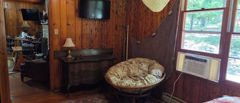 L’intérieur d’un chalet en bois comprend un lit, un téléviseur, un hamac et une grande fenêtre.