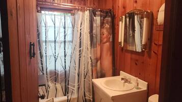 Une salle de bain avec une porte en bois, un rideau de douche orné d’un motif d’arbre, un lavabo avec un miroir et un porte-serviettes.