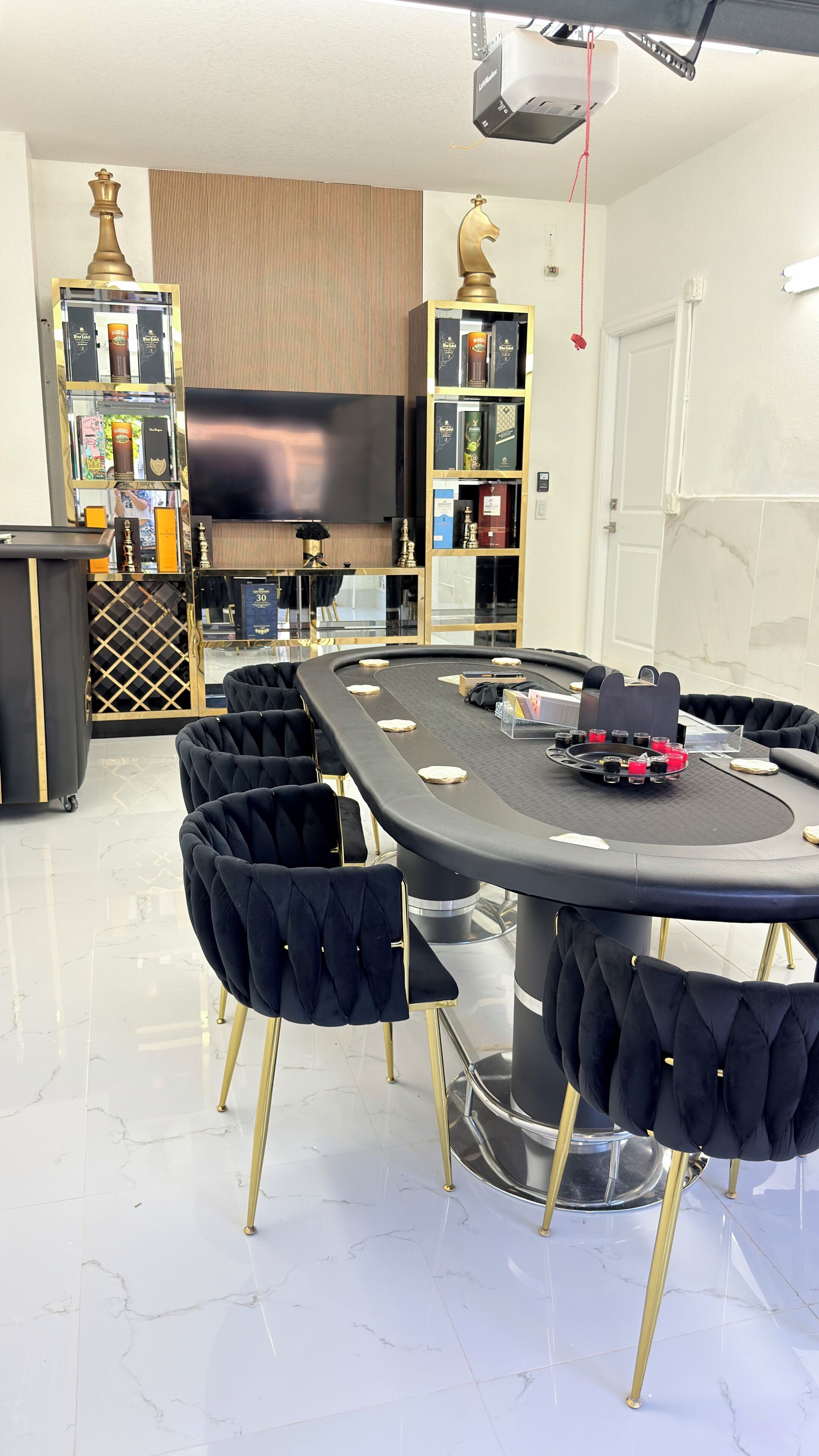 Un salon moderne avec une table ronde, des fauteuils noirs à revêtement en tissu, un téléviseur à écran plat et une bibliothèque contenant divers objets.