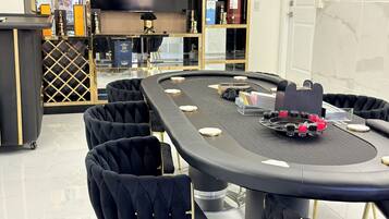 A modern living room with a round table, black upholstered chairs, a flat-screen TV, and a bookshelf with various items.