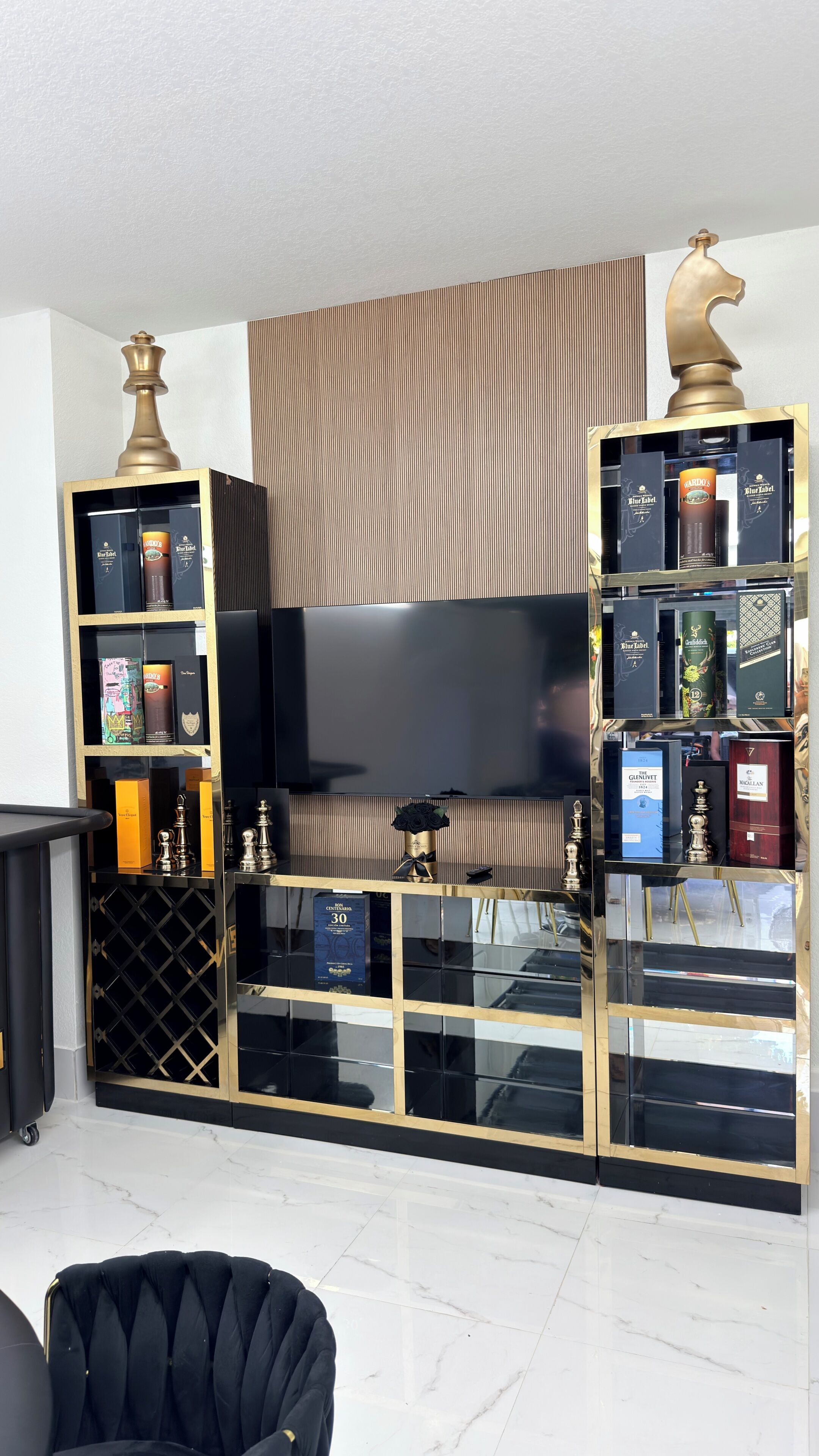 A modern living room with a large flat-screen TV, black and gold entertainment center, and a plush black sofa.