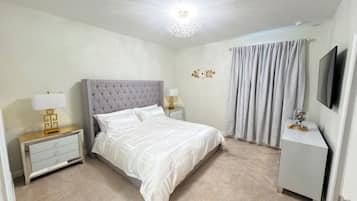 A neatly arranged bedroom with a bed, bedside tables, a lamp, a television, and a curtain.