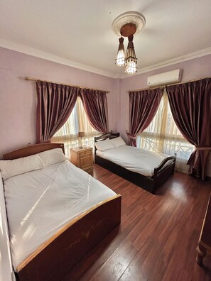Habitación de hotel con dos camas, suelo de madera, una mesita de noche y una lámpara en el techo.