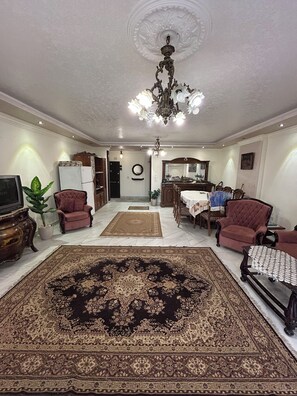 Un salón comedor amplio con un gran tapete decorado, una araña y una zona de comedor con mesa y sillas.