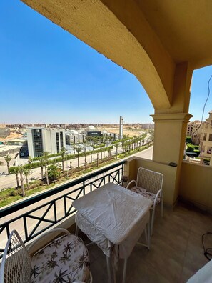 A balcony with a table and chairs, overlooking a cityscape with buildings and palm trees. - Luxury 3 bedroom Apartment in Rehab October City (Giza Governorate)