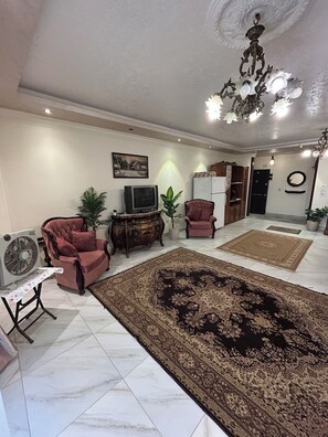 Una sala de estar con un tapete grande estampado, dos sillones, un televisor y una lámpara decorativa en el techo.
