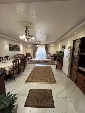 Une salle à manger spacieuse, agrémentée d’un lustre, d’un grand tapis et d’un réfrigérateur.