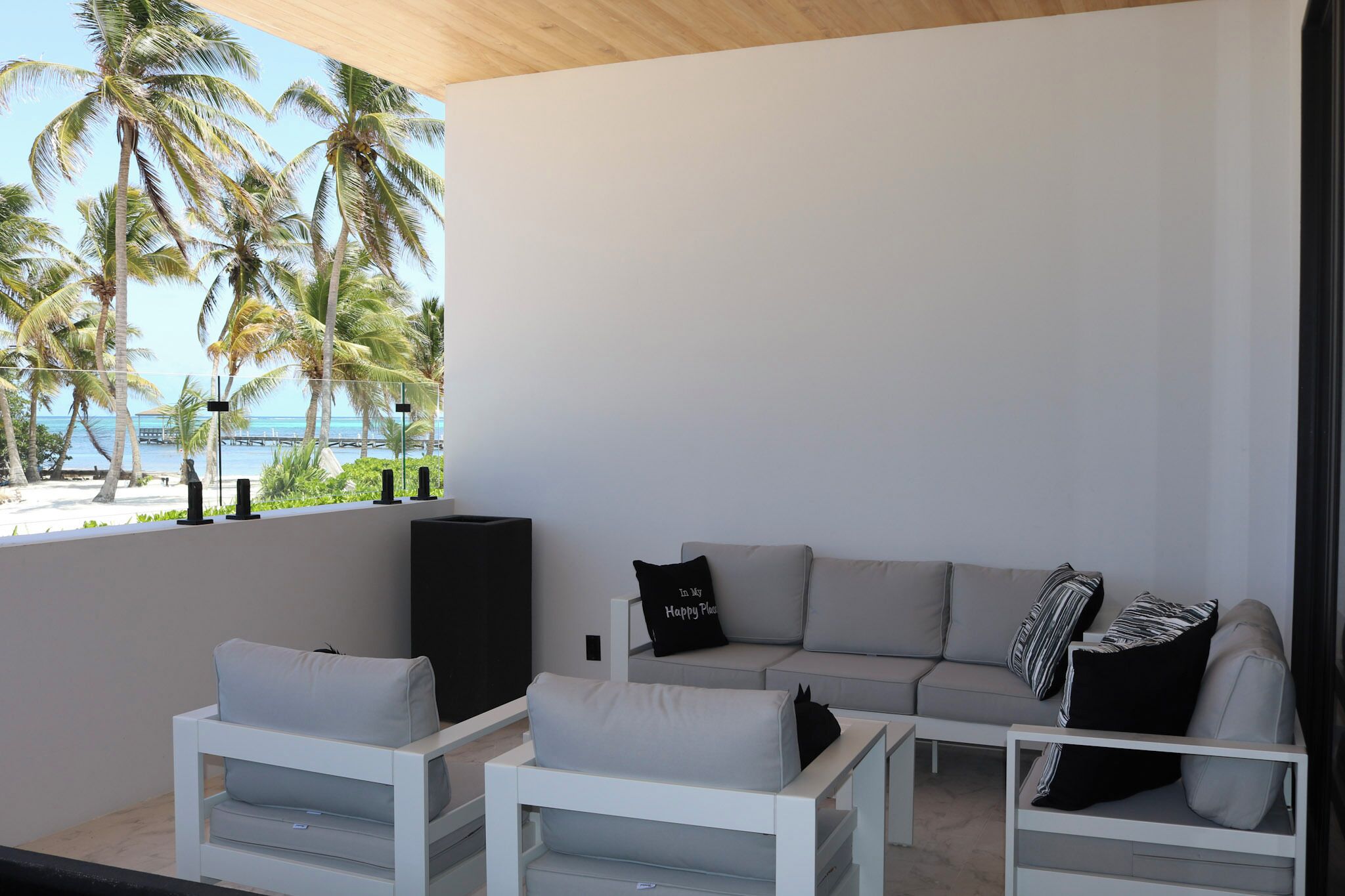 Un espace extérieur moderne, aménagé avec un canapé et des fauteuils, un téléviseur, et offrant une vue sur la plage et les palmiers.