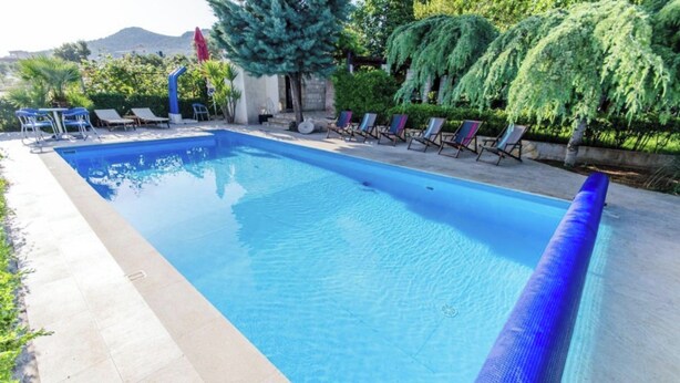 A rectangular swimming pool with clear blue water, surrounded by lounge chairs and a stone wall. - A 1  apt w shared pool and balcony, near the beach (Seget Vranjica)