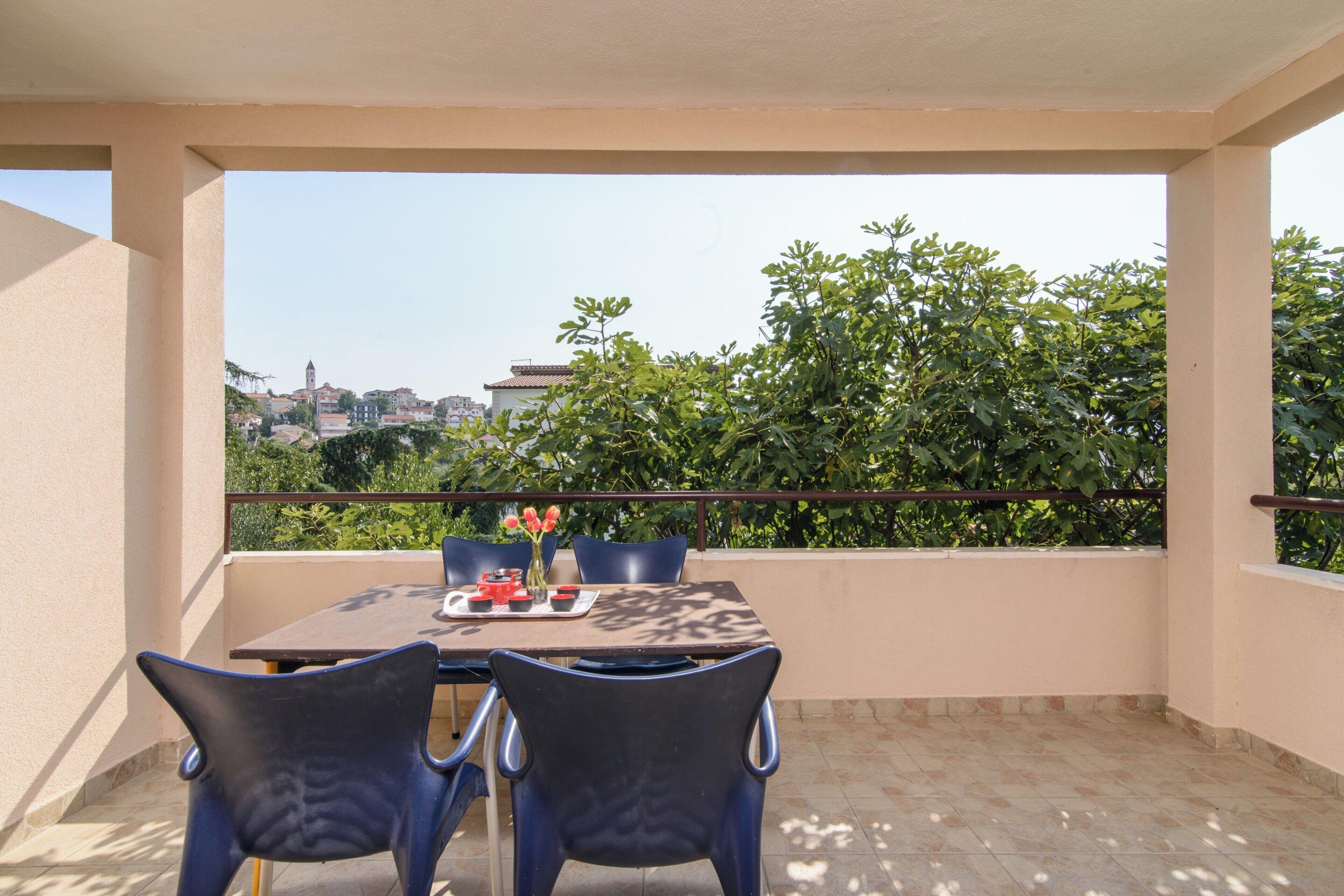 A balcony with a table and chairs, a vase with flowers, and a view of a cityscape.