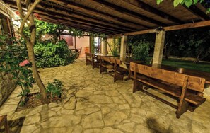 An outdoor patio area with stone flooring, wooden benches, and a covered section with a thatched roof. - A 1  apt w shared pool and balcony, near the beach (Seget Vranjica)