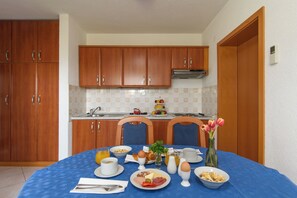 A kitchen with wooden cabinets, a stove, and a dining table set with breakfast items. - A 1  apt w shared pool and balcony, near the beach (Seget Vranjica)