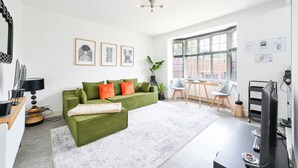 A modern living room with a green sofa, a coffee table, and a dining area with a table and chairs. - Emerald Garden Suite - Wifi,Parking,Garden,Sleep 2 (London)