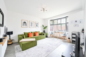 Uma sala de estar moderna com um sofá verde, uma mesa de centro e um espaço de jantar com uma mesa e cadeiras.