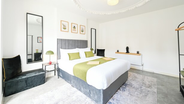 A modern hotel room with a large bed, a bedside table, a mirror, and a ceiling light. - Emerald Garden Suite - Wifi,Parking,Garden,Sleep 2 (London)