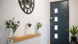 A hallway with a dark door, a radiator, and two potted plants on a shelf. - Emerald Garden Suite - Wifi,Parking,Garden,Sleep 2 (London)
