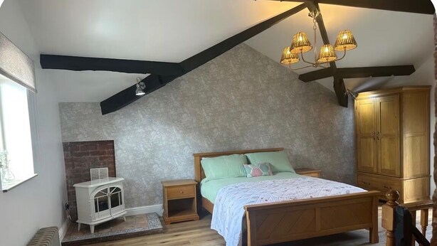 Une chambre avec un plafond en pente, un lit en bois, une table de chevet, une commode et un radiateur.