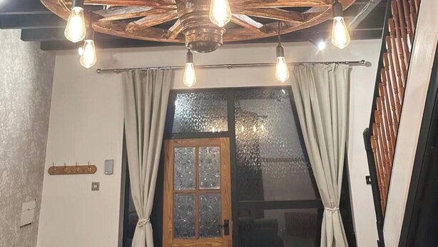 Habitación con ventilador de techo de madera, puerta de madera con paneles de vidrio esmerilado y lámpara con bombillas expuestas.
