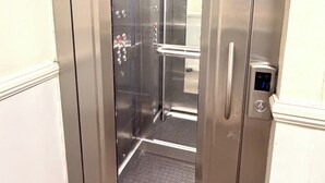 An elevator with a metallic finish, a handrail, and a control panel with directional arrows. - Cozy London Apartment with City Views (London)