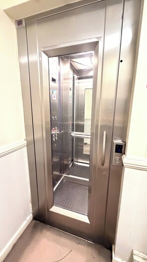 An elevator with a metallic finish, a handrail, and a control panel with directional arrows. - Cozy London Apartment with City Views (London)