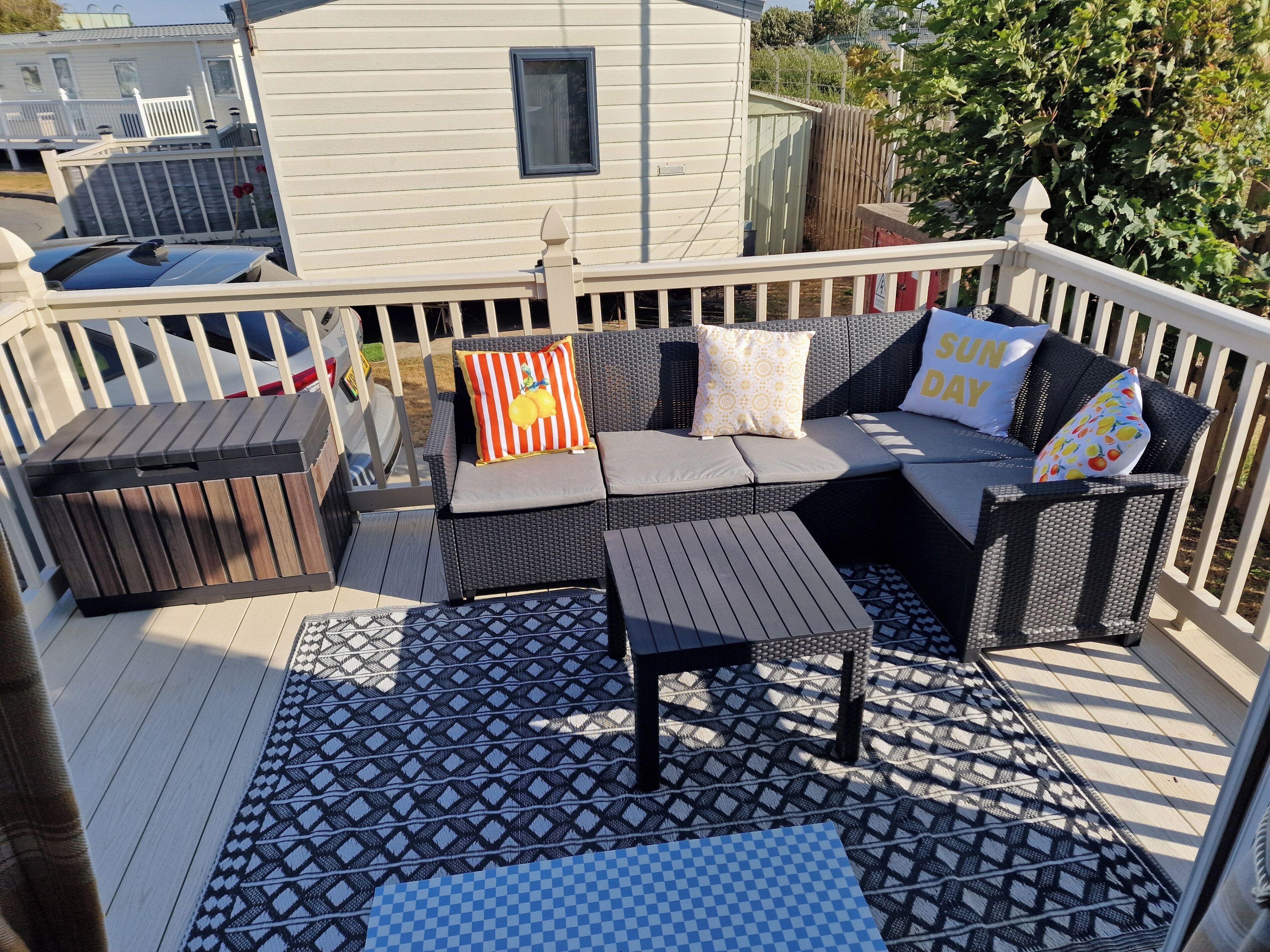 A deck with outdoor furniture, including a sofa and a table, and a patterned rug.