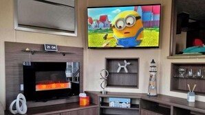 Een moderne woonkamer met een flatscreen televisie aan de muur, een open haard en een klein plankje met decoratieve objecten.