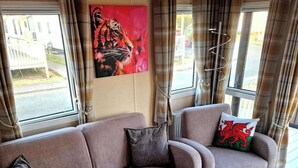 Een woonkamer met een bank, twee kussens, een schilderij en een raam met gordijnen.