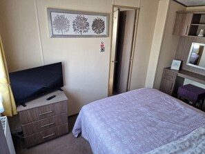 Quarto de hotel com uma cama, televisão, cômoda, espelho e porta que dá para outro quarto.