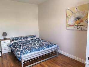 A bedroom with a bed, a nightstand, a lamp, and a painting on the wall.