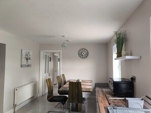 A modern kitchen with a dining area, white walls, a clock, and a radiator.