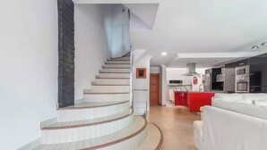 A modern interior with a curved staircase, a kitchen area with red accents, and a white sofa. - Casa Encanto Arinaga (Aguimes)