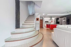 Um interior moderno com uma escada curva, uma área de cozinha com detalhes vermelhos e um sofá branco.