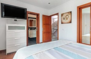 Quarto com cama, televisão, guarda-roupa e porta para uma casa de banho.
