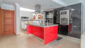 A modern kitchen with a central island, built-in appliances, and a dining area with chairs. - Casa Encanto Arinaga (Aguimes)
