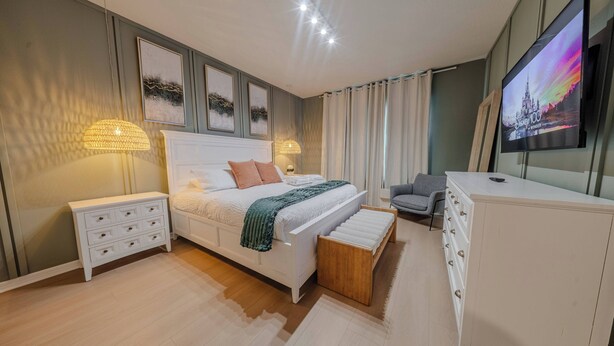 Une chambre à coucher avec un lit, des tables de chevet, un téléviseur et des œuvres d’art accrochées au mur.