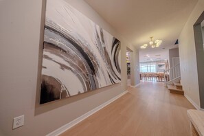 Un couloir orné d’un grand tableau abstrait, avec un escalier et, au fond, un coin repas.