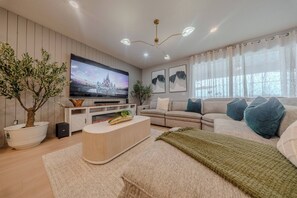 Ein modernes Wohnzimmer mit Flachbildfernseher, einer Sofagarnitur, einem Couchtisch und Zimmerpflanzen.