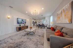 A modern living room with a flat-screen TV, a dining area, and a kitchen in the background. - Go!#41 - WINDSOR AT WESTSIDE (Kissimmee)
