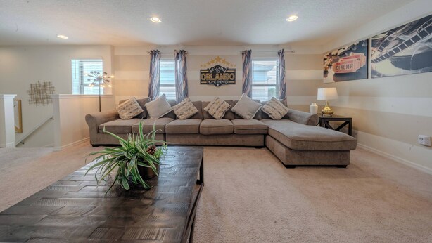 A living room with a sectional sofa, a coffee table, and a wall-mounted lamp. - Go!#41 - WINDSOR AT WESTSIDE (Kissimmee)