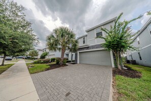 A residential driveway with a paved walkway, a garage, and a row of houses with a clear sky above. - Go!#41 - WINDSOR AT WESTSIDE (Kissimmee)