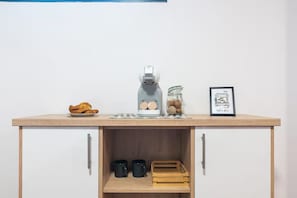 Eine Küchenzeile mit Kaffeemaschine, einer Kaffeebohnen-Glaseinlage, einer gerahmten Illustration einer Kaffeebar und einem Teller Croissants.