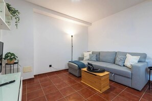 Ein Wohnzimmer mit grauem Sofa, einem Holztisch, einer Stehlampe und einem Fernseher auf einem Schrank.