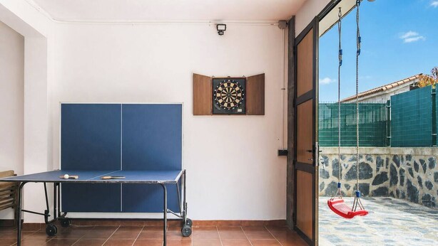 A room with a ping pong table, a dartboard, and a view of a swimming pool area. - Casa De Invitados El Rincon De Itara (Firgas)