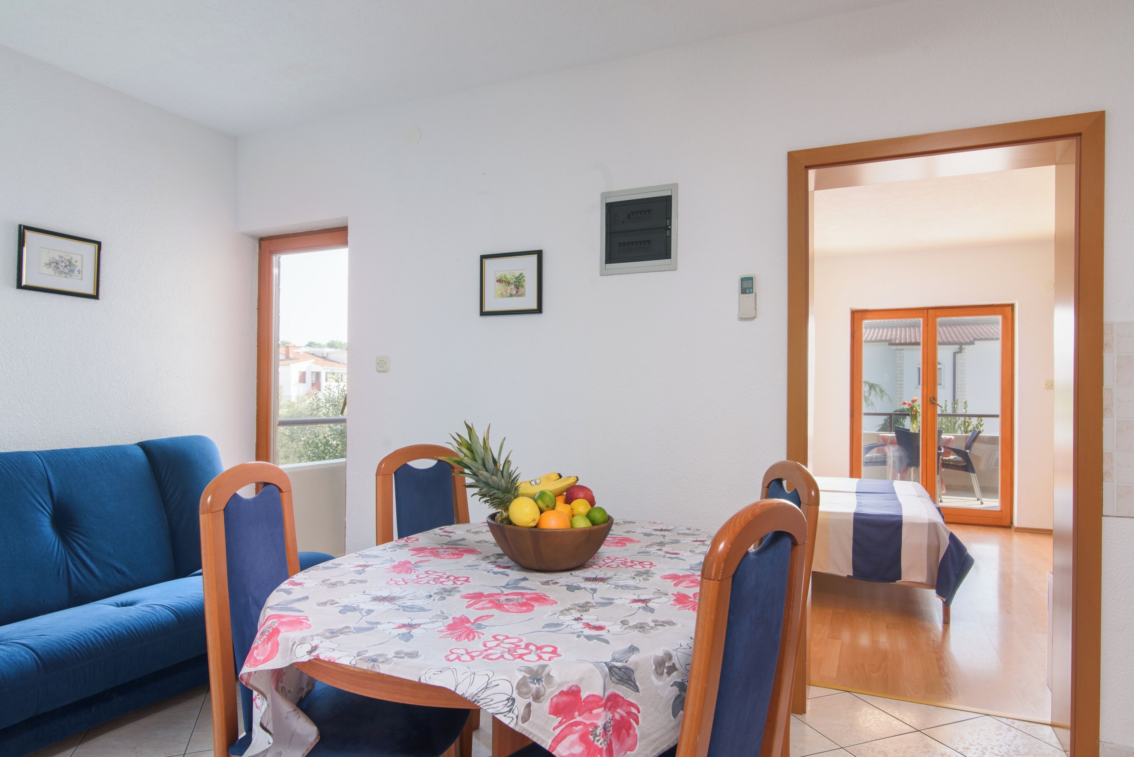 Un coin repas avec une table dressée pour deux personnes, un canapé bleu et un panier de fruits posé sur la table.