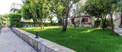 A stone pathway leading to a grassy area with trees and a stone building.