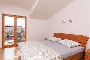 Quarto com cama, duas almofadas, cabeceira de madeira, mesa de cabeceira e porta de vidro deslizante que dá para uma área externa.