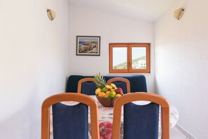 Ein Essbereich mit Tisch für vier Personen, einer Obstschale auf dem Tisch, einem gerahmten Bild an der Wand und einem Fenster mit Blick auf Gebäude.