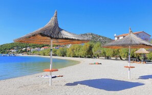 A beach with thatched umbrellas, a pebble beach, and a backdrop of houses and trees. - A 4 apt w shared pool and balcony, near the beach (Seget Vranjica)