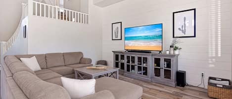 Una sala de estar con un sofá seccional, una mesa de centro, un televisor sobre un mueble bajo y una escalera.